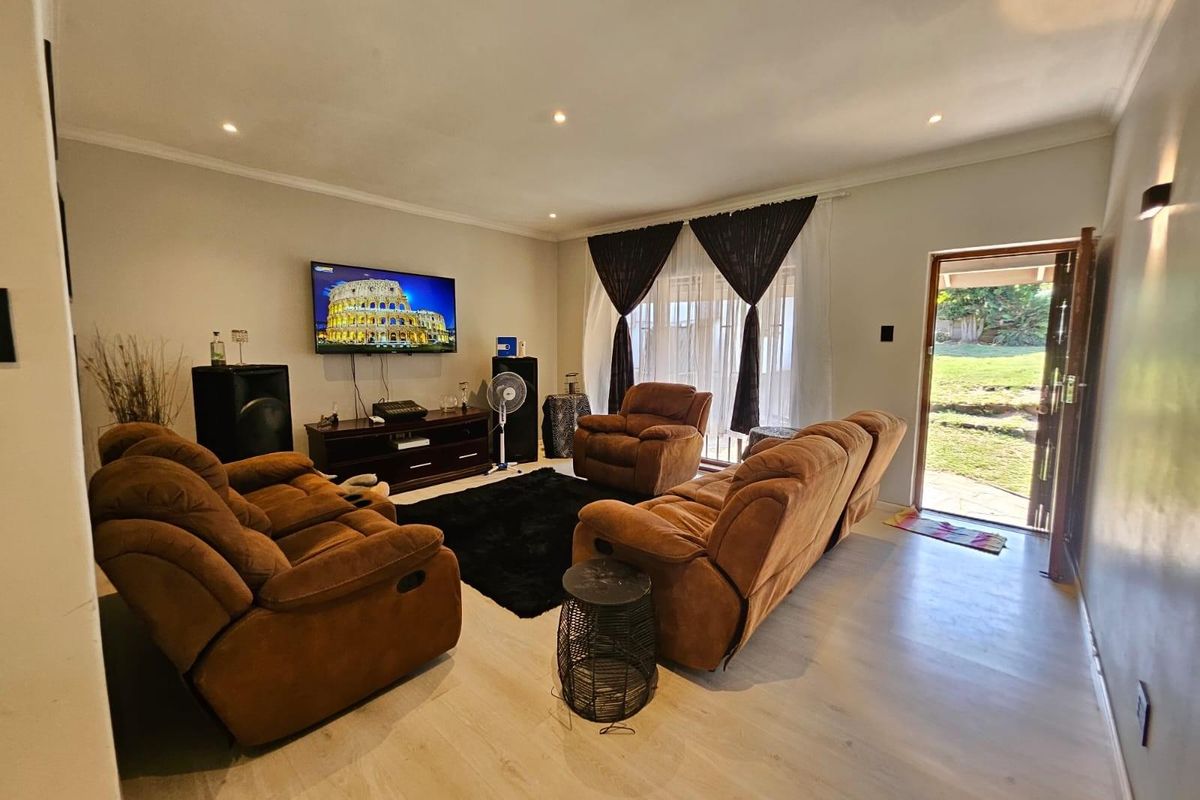 A spacious living room featuring light-toned laminate flooring, recessed downlighting, and direct access to the rear garden through a sliding glass door.