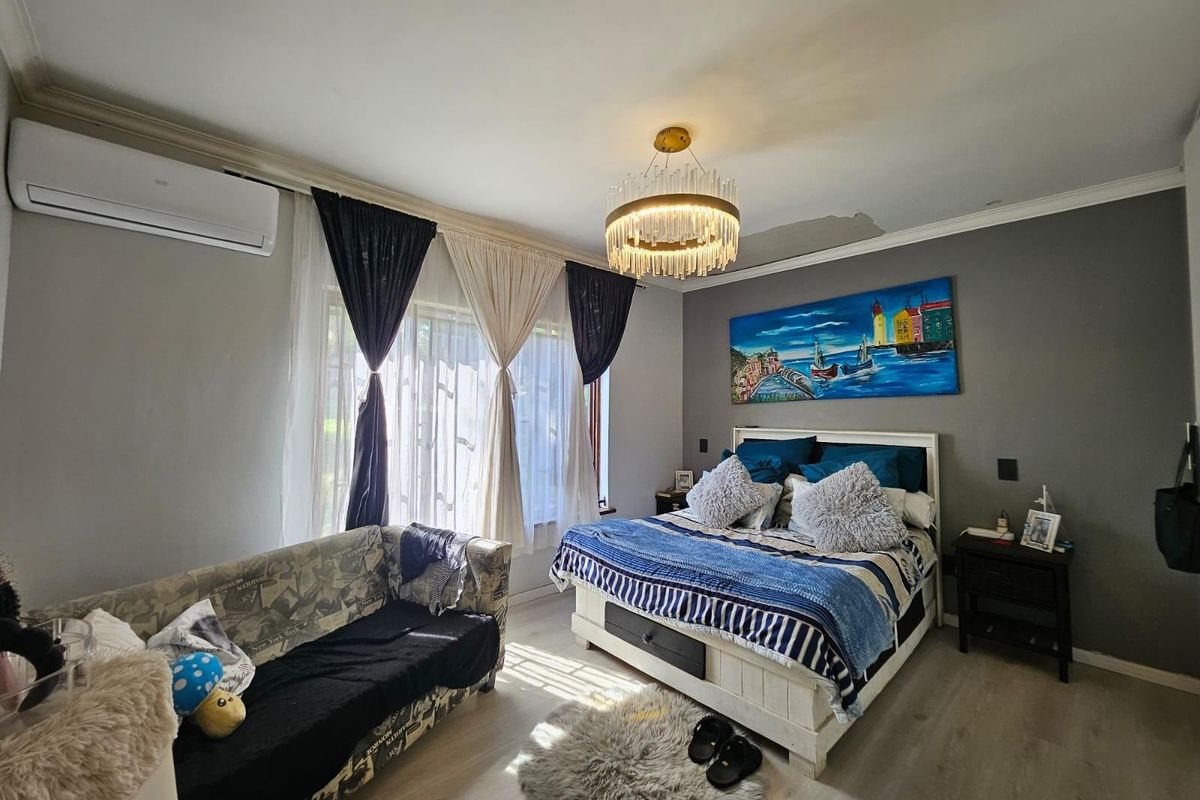 A bedroom featuring laminate flooring, cove molding, and a split-system air conditioner, with visible ceiling water damage requiring repair.