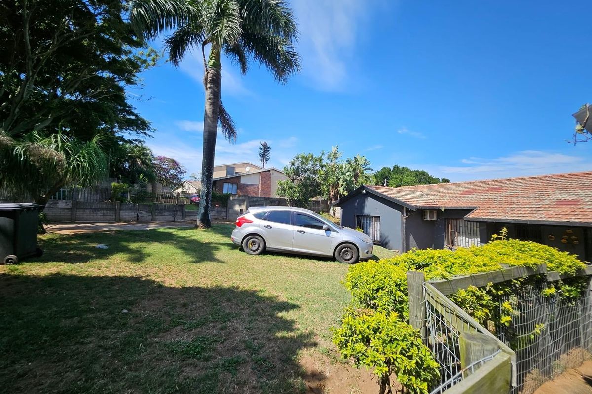 Rear exterior view of the property featuring a tiled roof, perimeter wall, and established garden area.