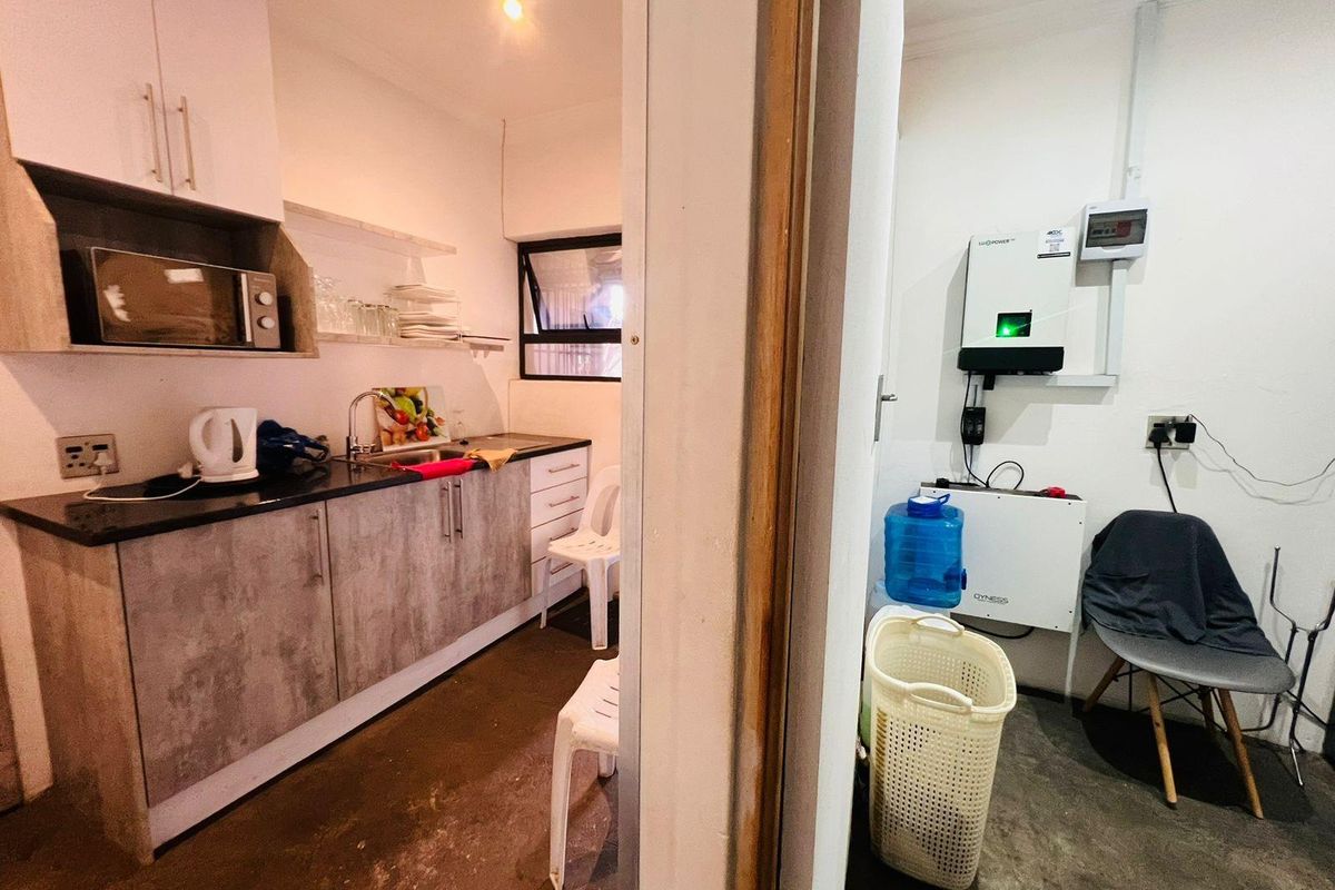 A compact kitchenette featuring built-in cabinetry and sink, adjacent to a utility space housing a solar inverter system and electrical distribution board.