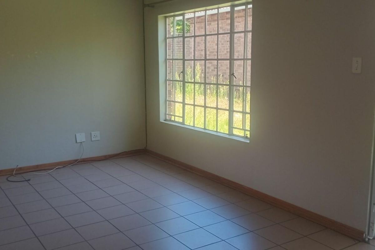 An empty living room featuring tiled flooring, a large window with security bars, and a sliding door leading to an outdoor area.