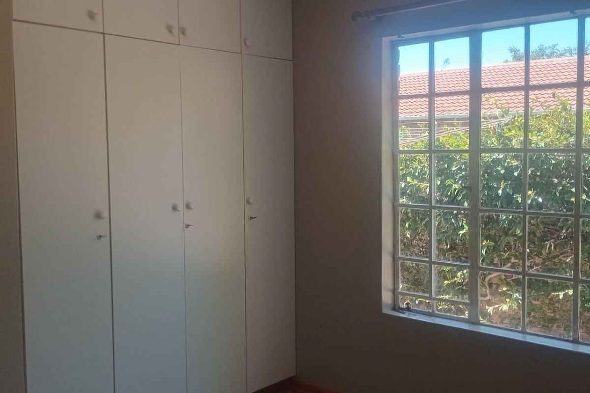 A bright bedroom featuring built-in floor-to-ceiling cabinetry and a large window with security bars overlooking the garden.