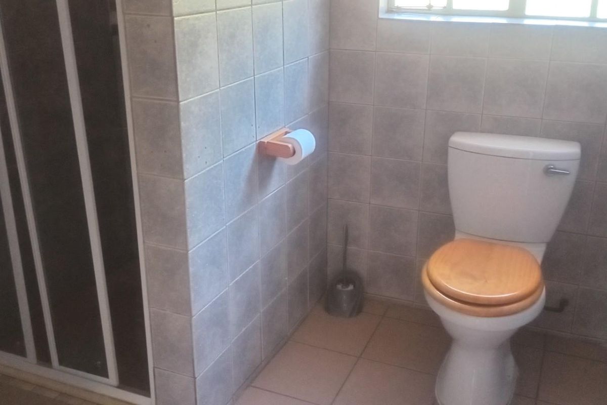 A functional bathroom featuring a tiled shower enclosure and a standard toilet with neutral wall and floor tiling.