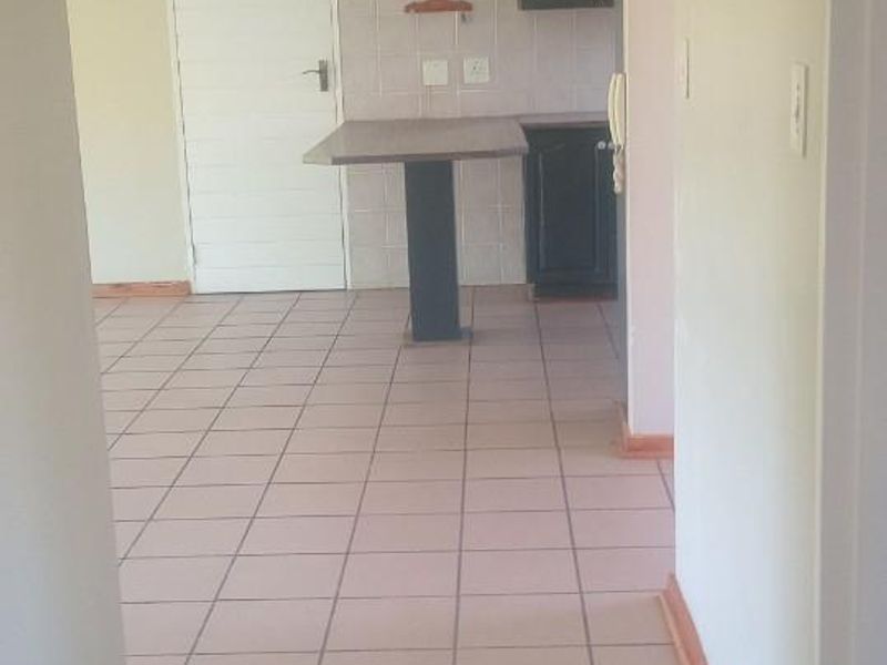 A view from a hallway looking into an open-plan kitchen area featuring tiled flooring and built-in cabinetry.