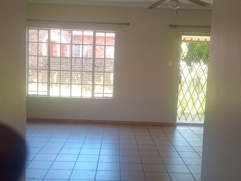 An empty living area featuring tiled flooring, a ceiling fan, and a security gate leading to the exterior.