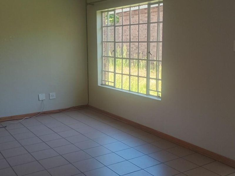 An empty living room featuring tiled flooring, a large window with security bars, and a sliding door leading to an outdoor area.