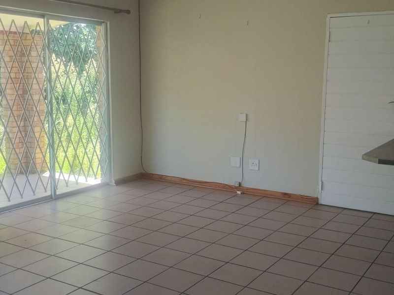 An open-plan living area featuring tiled flooring, a built-in breakfast bar, and a sliding glass door with security gate leading to the exterior.