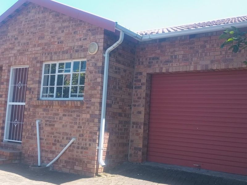 Front elevation of a face-brick townhouse featuring a single garage with a red roller door and a secure entrance.