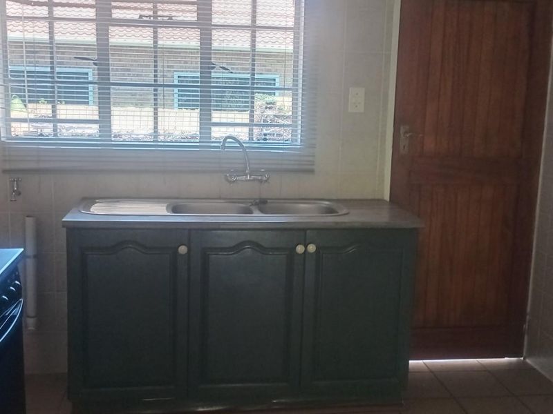 A functional kitchen area featuring a double stainless steel sink, built-in cabinetry, and a standalone electric stove.