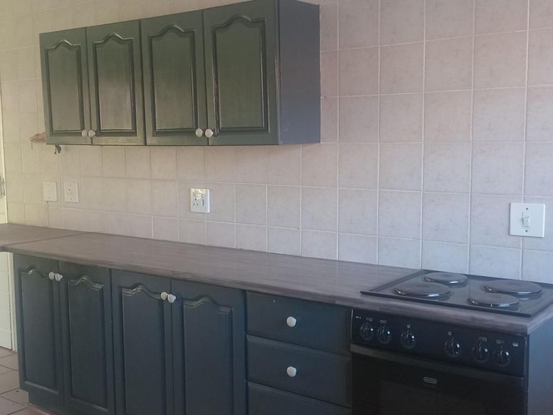 A functional kitchen area featuring dark-painted cabinetry, a built-in electric stove and oven, and tiled wall splashbacks.