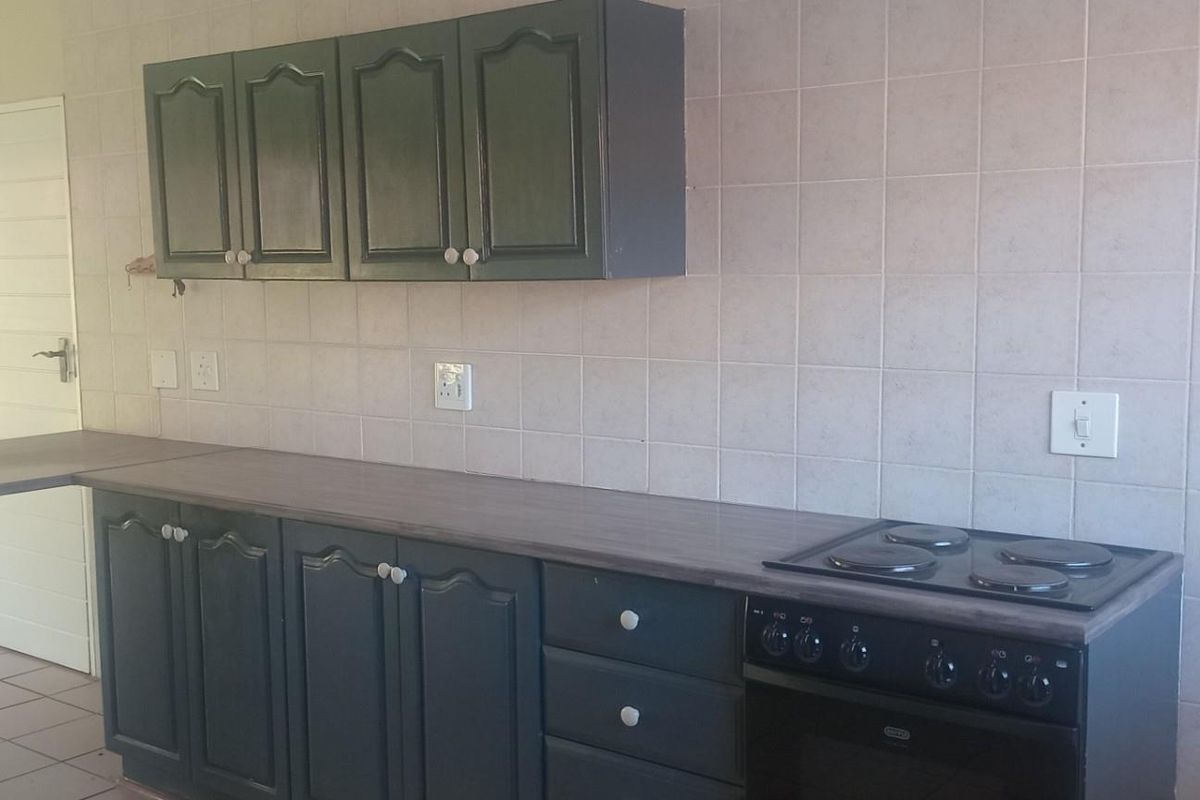 A functional kitchen area featuring dark-painted cabinetry, a built-in electric stove and oven, and tiled wall splashbacks.