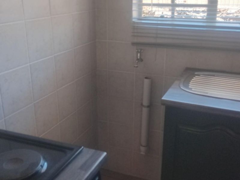 A functional kitchen area featuring a built-in electric hob, stainless steel sink with drainer, and tiled splashbacks.