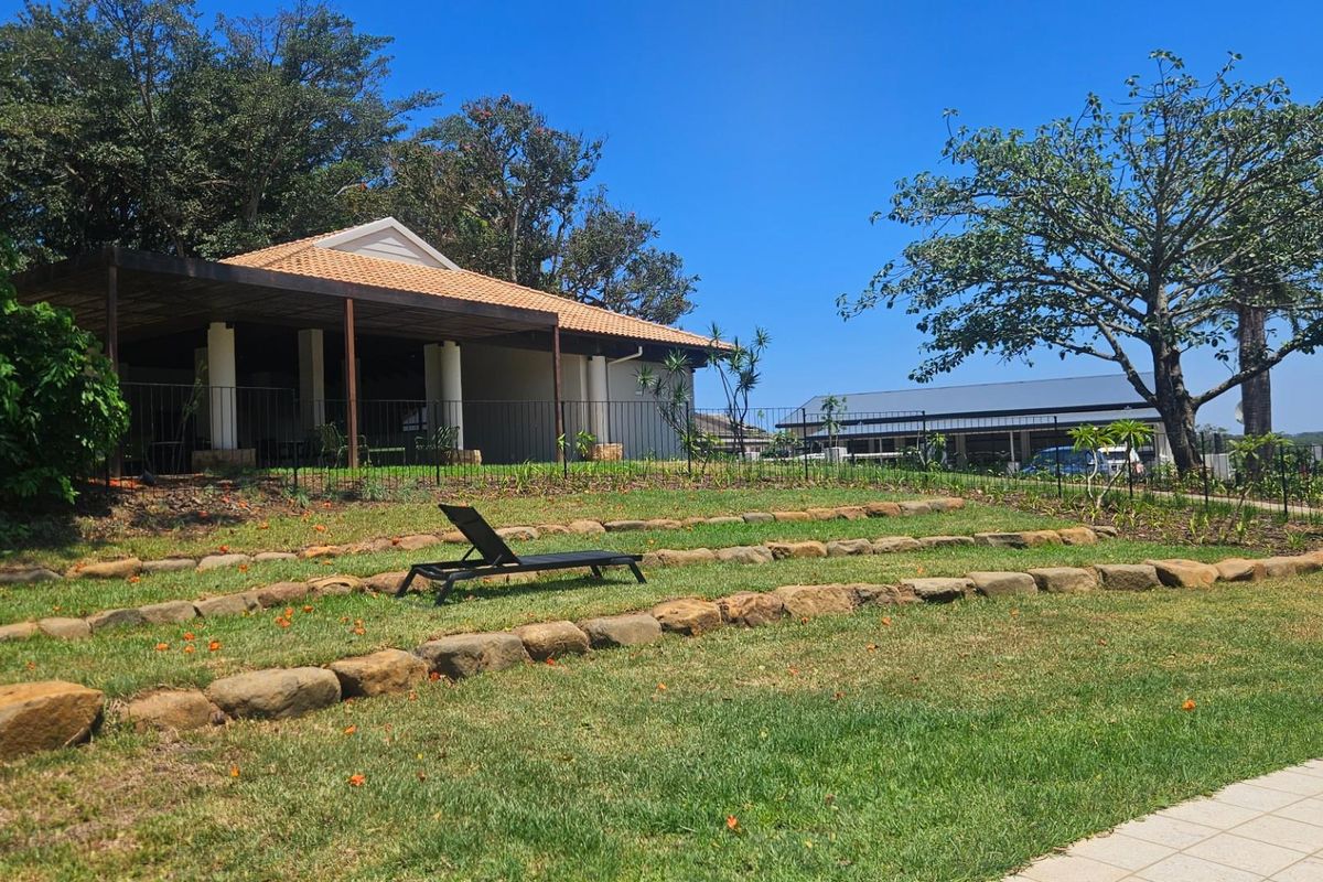 A well-maintained rear garden featuring a terraced lawn with stone retaining walls, leading to a covered patio area with a tiled roof.