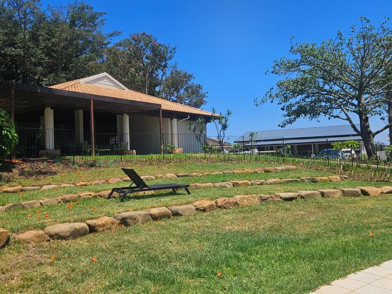 A well-maintained rear garden featuring a terraced lawn with stone retaining walls, leading to a covered patio area with a tiled roof.
