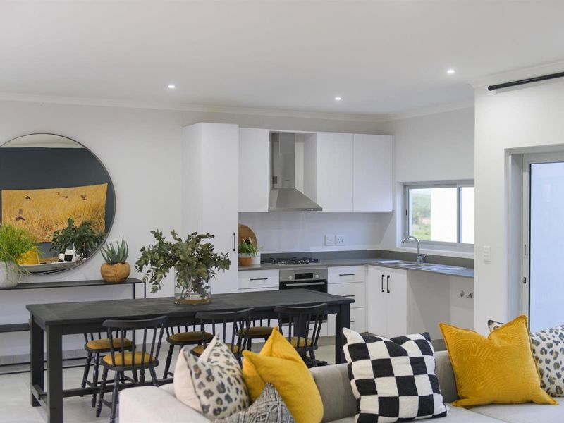 Modern open-plan kitchen and dining area featuring sleek white cabinetry, integrated appliances, and recessed lighting, creating a bright and functional living space.