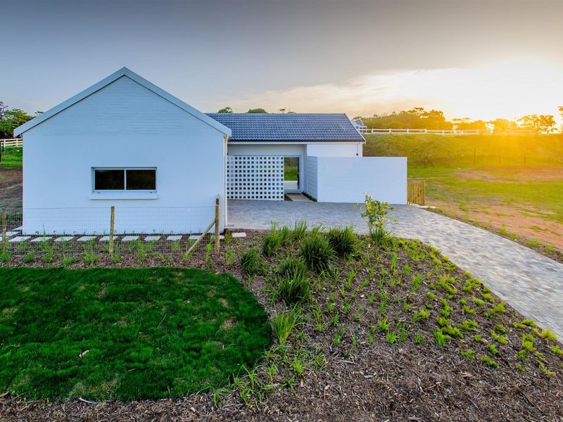 A modern white residential property featuring a paved driveway, breeze block architectural detail, and a well-maintained garden at sunset.