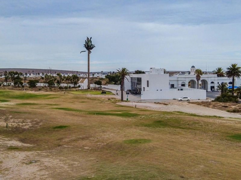 An aerial view of a residential golf course estate featuring landscaped grounds, mature palm trees, and nearby white architectural structures.