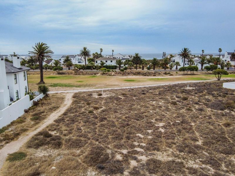 An aerial view of a vacant residential plot featuring natural coastal vegetation, adjacent to established residential properties and near the coastline.