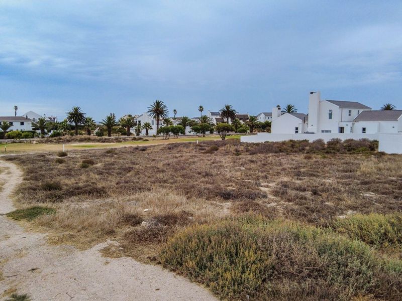 A view of a vacant residential plot featuring natural vegetation, situated within a developed coastal estate.