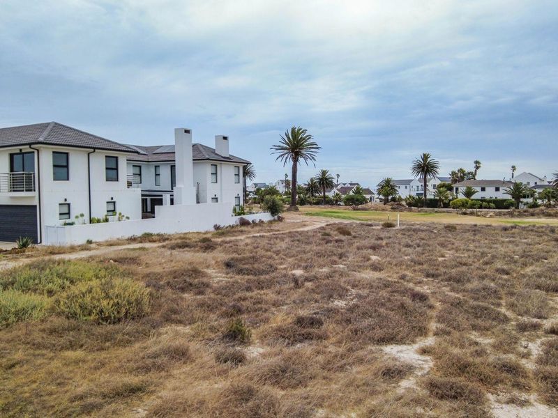 Aerial view of a vacant residential plot adjacent to an existing modern two-story home in a coastal estate setting.