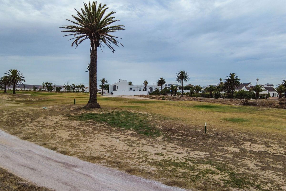 An aerial view of a residential vacant land plot situated within a golf estate, featuring established palm trees and surrounding neighborhood views.