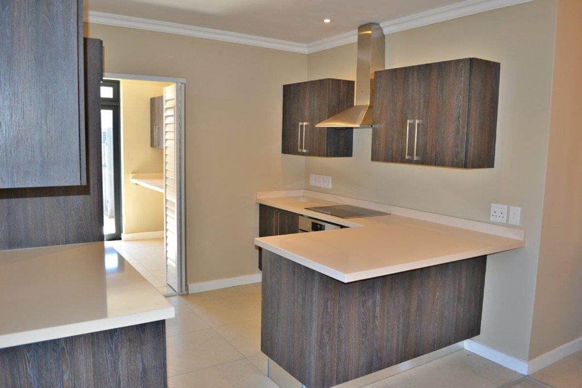 Modern kitchen featuring dark wood-grain cabinetry, stone countertops, integrated hob, and stainless steel extractor fan, with an adjacent scullery area.