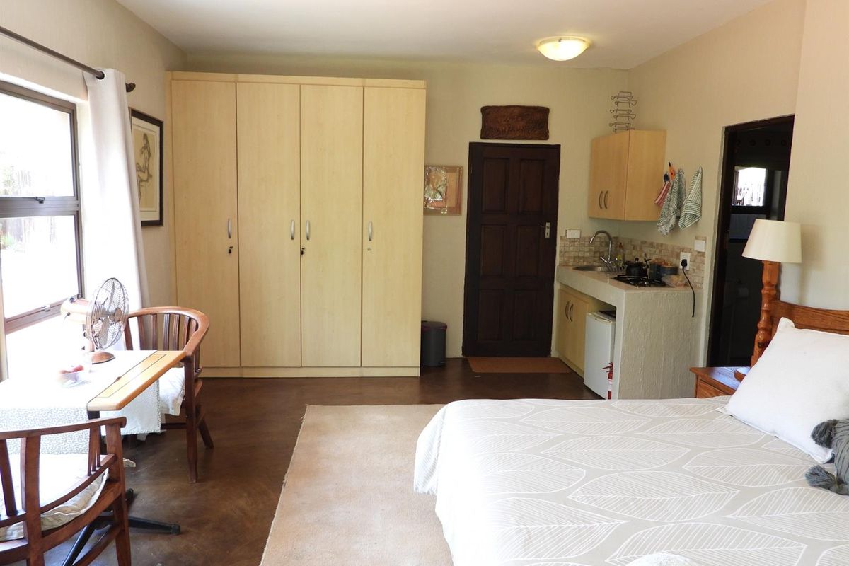 A bedroom featuring built-in cupboards and a compact kitchenette with a sink and tiled splashback, finished with concrete flooring.