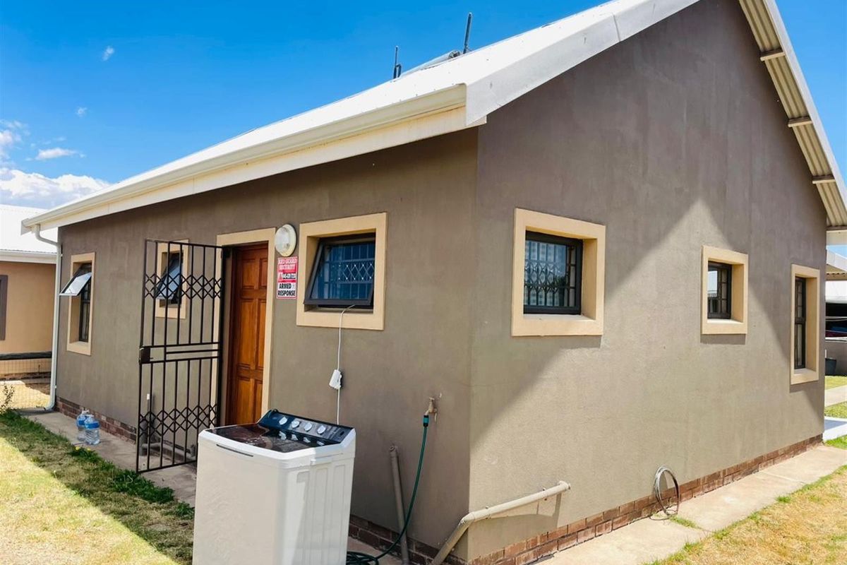 A view of the rear exterior of the house featuring plastered walls, security gates, and window bars.
