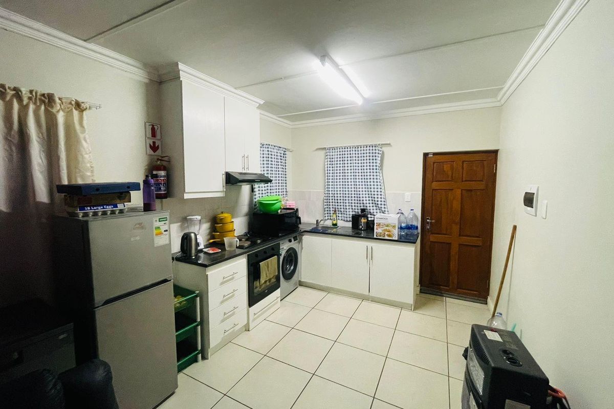 A functional kitchen featuring white cabinetry, dark countertops, tiled flooring, and integrated appliances, providing a practical workspace with direct exterior access.