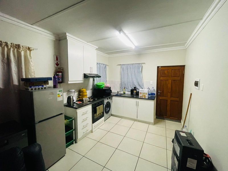 A functional kitchen featuring white cabinetry, dark countertops, tiled flooring, and integrated appliances, providing a practical workspace with direct exterior access.