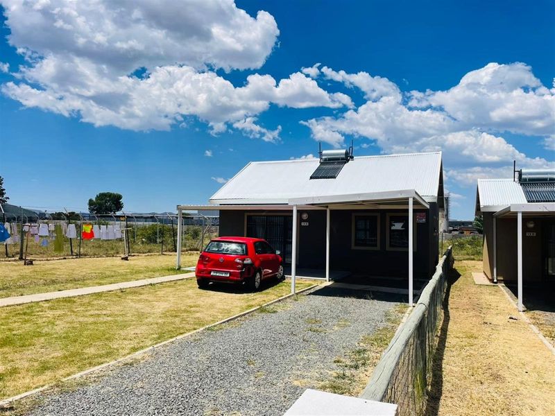 Front view of a detached house featuring a gravel driveway, covered patio area, and a roof-mounted solar water heating system.