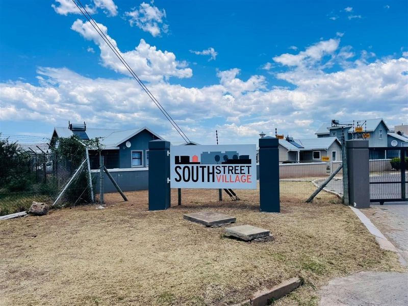 Entrance view of South Street Village featuring security gate, perimeter fencing, and residential units with solar water heaters.