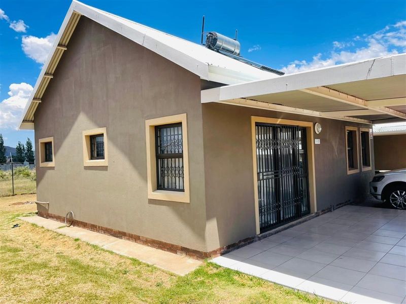 Front exterior view of the house featuring a carport, tiled patio area, solar water heating system, and secure window and door fittings.