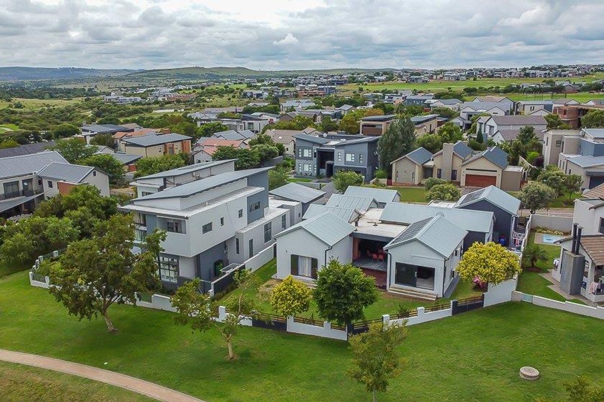 Aerial view of a modern residential property featuring a metal roof, landscaped garden, and boundary wall within a suburban estate setting.