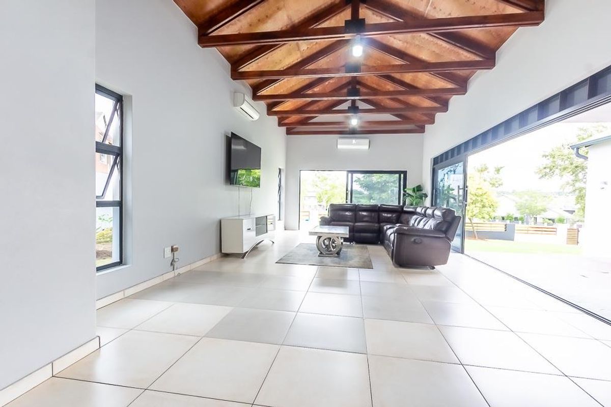 Spacious living area featuring high exposed timber truss ceilings, large format floor tiles, and expansive sliding glass doors opening to the exterior.