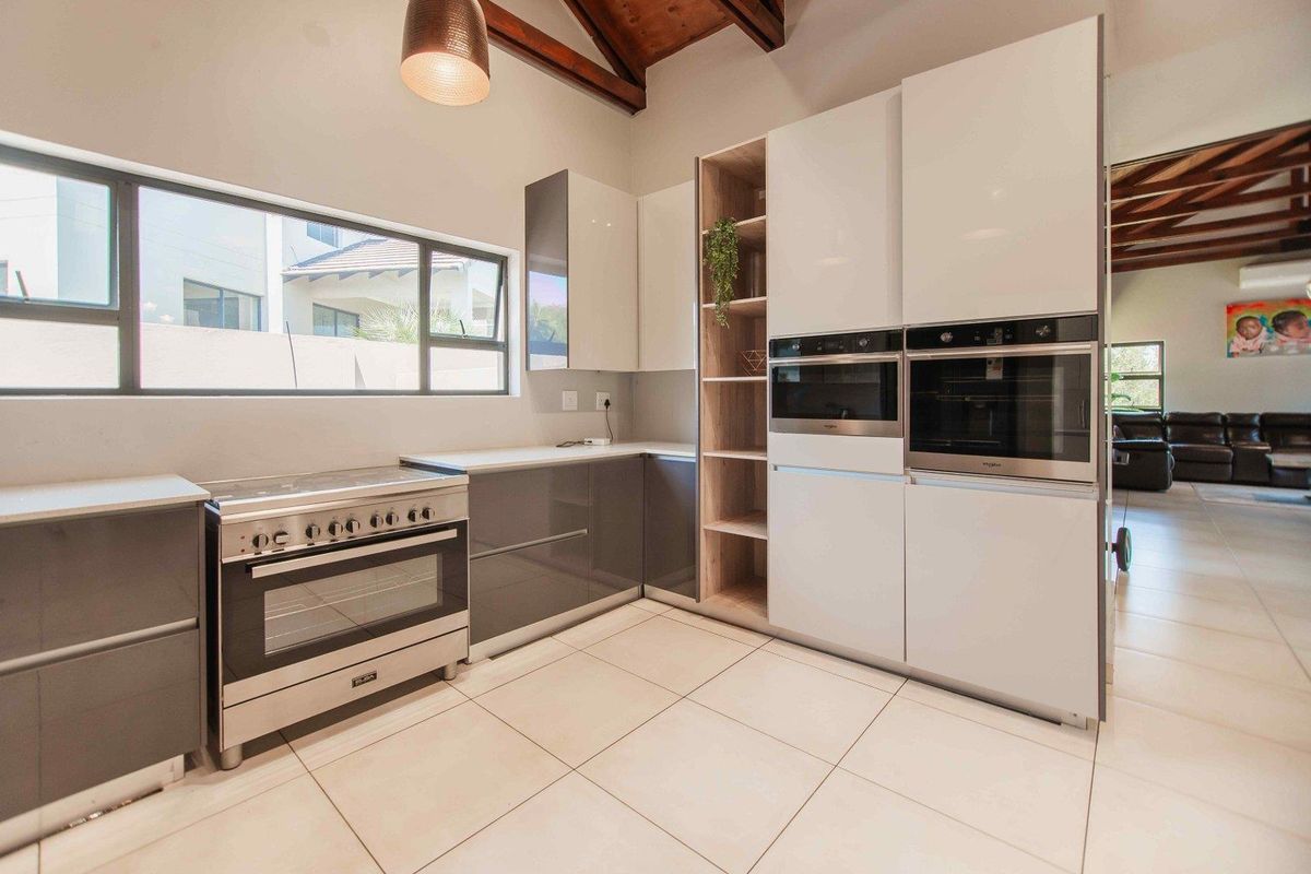 Modern kitchen featuring high-gloss cabinetry, built-in appliances, a freestanding stove, and striking exposed timber ceiling beams.