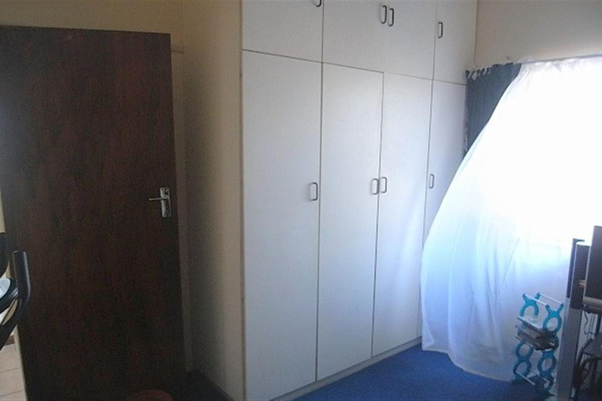 A bedroom featuring floor-to-ceiling built-in cupboards and carpeted flooring, providing ample storage space.