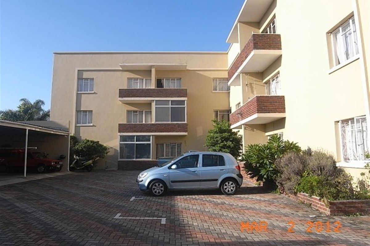 Exterior view of an apartment complex featuring a paved parking area, carports, and balconies with brick accents.