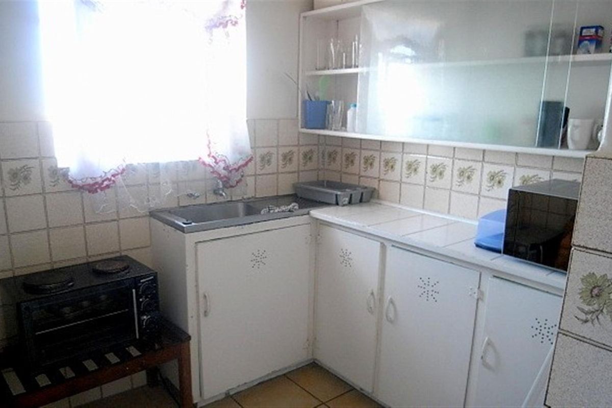 A compact, dated kitchen featuring white built-in cabinetry, a double sink, and tiled backsplash, offering potential for a modern renovation.