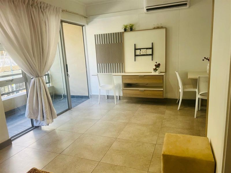 A bright living area featuring tiled flooring, a built-in wall unit, and a sliding glass door providing access to an outdoor balcony.