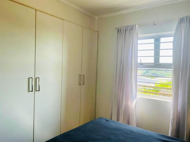 A bedroom featuring built-in cupboards and a window with security bars, providing natural light and storage space.