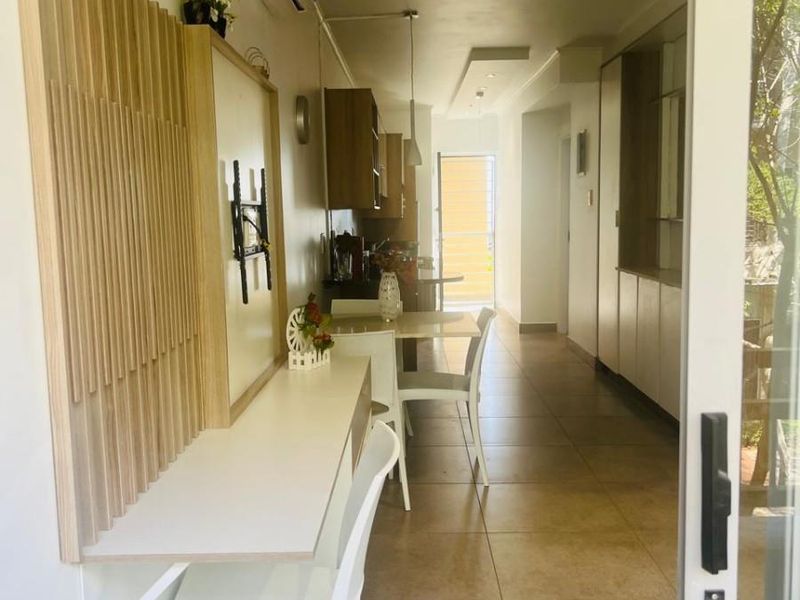 An open-plan living and kitchen area featuring tiled floors, built-in cabinetry, a wall-mounted desk, and a split-system air conditioner, leading to an outdoor space.