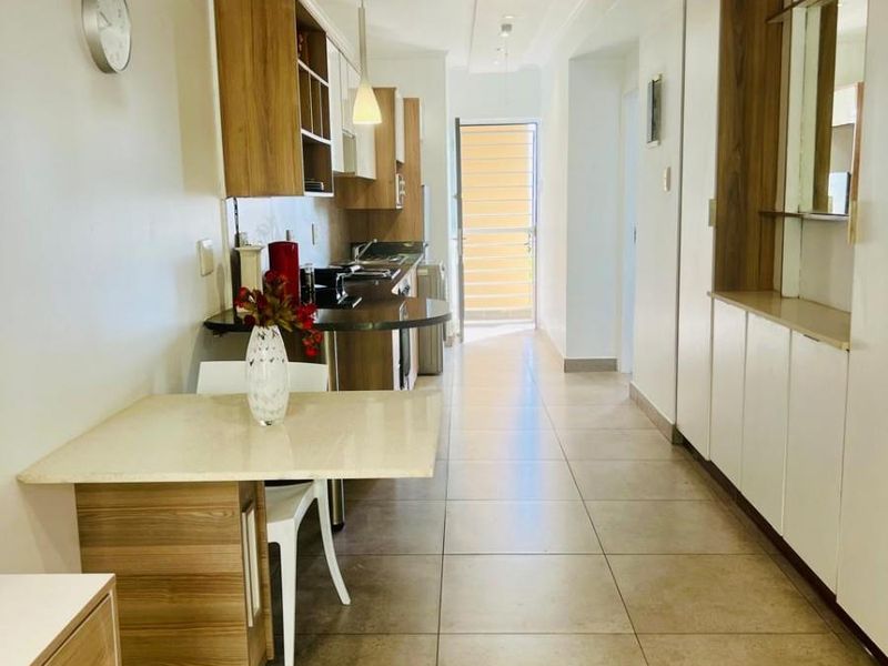 A functional kitchen featuring built-in cabinetry, stone countertops, and ceramic floor tiles, leading to an exterior doorway with natural light.