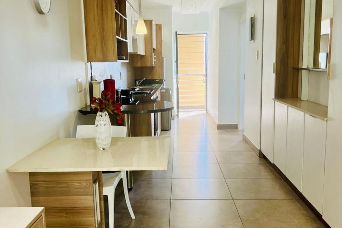 A functional kitchen featuring built-in cabinetry, stone countertops, and ceramic floor tiles, leading to an exterior doorway with natural light.