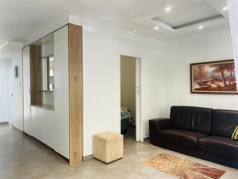 A well-maintained living area featuring modern tiled flooring, a recessed ceiling with downlights, and custom built-in cabinetry with wood-grain accents.