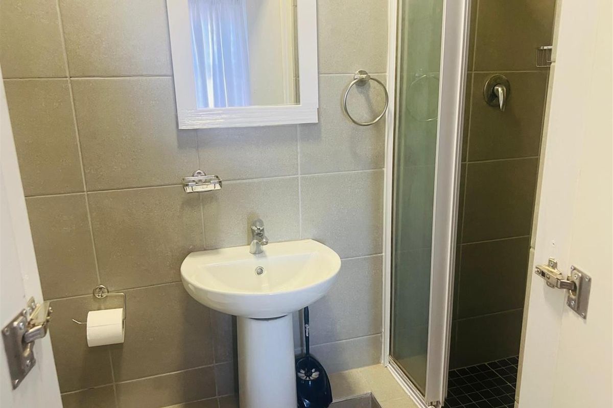 A compact bathroom featuring a pedestal washbasin, a shower enclosure with tiled walls, and essential fixtures in a neutral color palette.