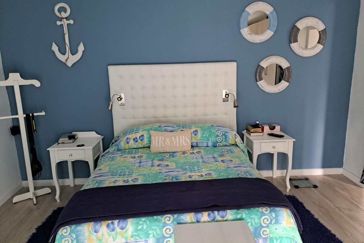 A bedroom featuring a tufted headboard with integrated reading lights, set against a blue accent wall with light-toned wood-look flooring.