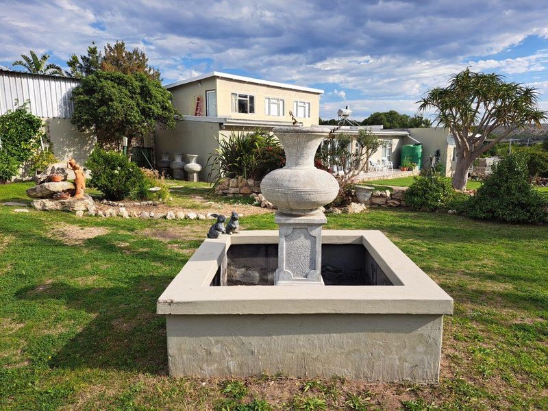 A view of the rear garden featuring a central stone fountain, landscaped lawn, and the rear elevation of the farm dwelling.