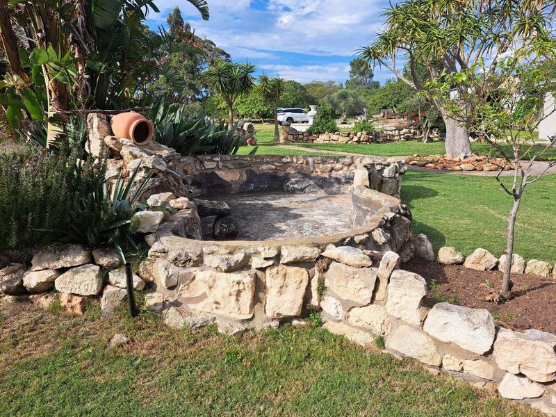A rustic stone-built garden feature with integrated planter and decorative pottery, set within a well-maintained farm landscape.