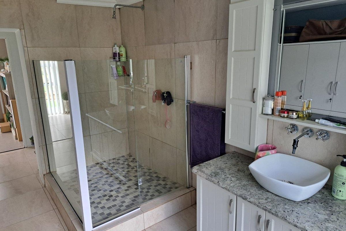 A well-maintained bathroom featuring a glass-enclosed walk-in shower with mosaic tile flooring, a granite-topped vanity, and built-in cabinetry.
